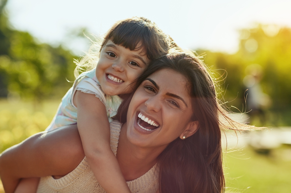 Smiling mother giving her daughter a piggyback ride outdoors