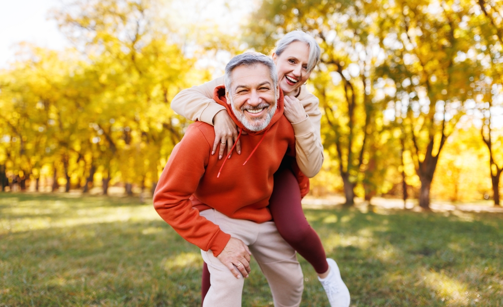 Smiling older man giving a woman a piggyback ride in an autumn park